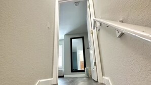 Una escalera con acabado de madera oscura y barandas blancas que conduce a una habitación con un ventanal y una puerta.