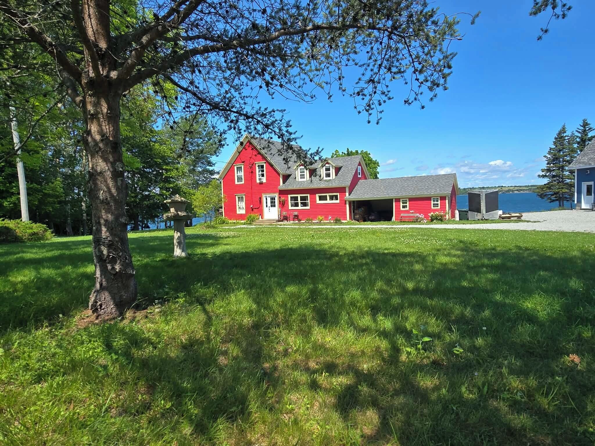 A red two-story house with a garage, surrounded by a grassy yard and a body of water.