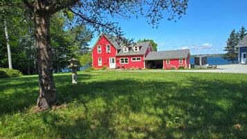 A red two-story house with a garage, surrounded by a grassy yard and a body of water.