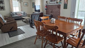 A living room with a fireplace, a television, a dining table with chairs, and a sofa. - Rustic waterfront farmhouse on Sydney Harbour, with amazing sunset views. (Point Edward)