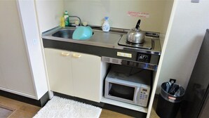 A compact kitchenette with a sink, kettle, microwave, and storage cabinets. - Hotel Stay Inn San Annex (Yamagata)