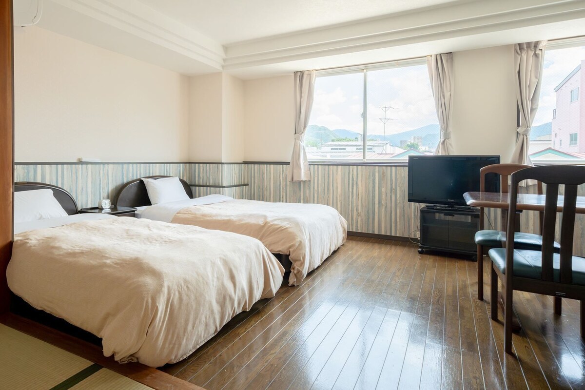 A hotel room with two beds, a television, and a desk with a chair.
