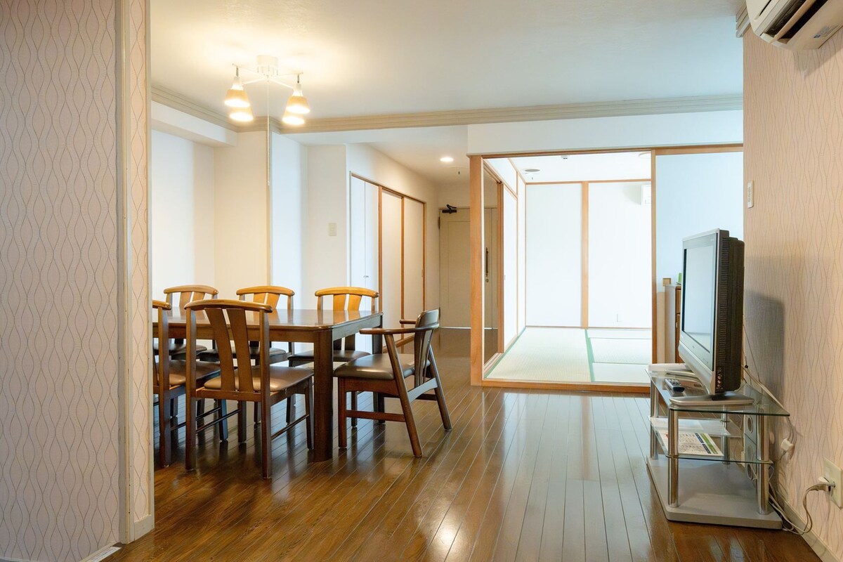 A room with a dining table, chairs, a television, and a sliding door leading to a balcony.