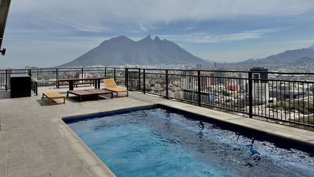 A rooftop pool with lounge chairs and a view of a mountain.