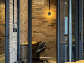 Un espacio de oficina moderno con pared de ladrillo, lámpara redonda y separador de vidrio con una silla.