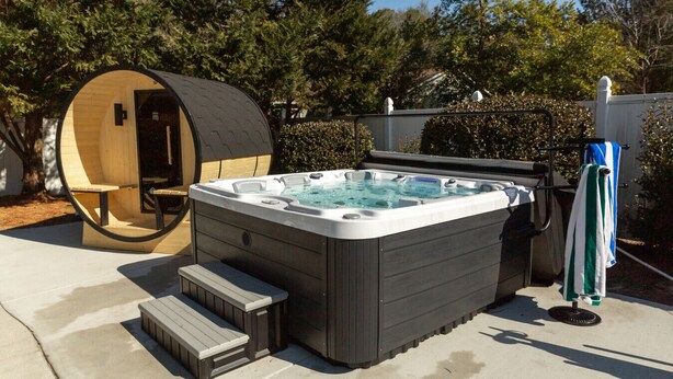 A hot tub with steps leading up to it, a wooden sauna, and a towel rack with a towel. - Golfer Paradise - Pool, Sauna, Hot Tub, Putting Green and More! (Pinehurst)