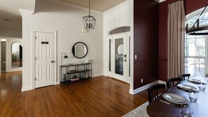 A dining area with a wooden table set for four, a black console table with a mirror and books, and a view of the outdoors through a window. - Golfer Paradise - Pool, Sauna, Hot Tub, Putting Green and More! (Pinehurst)