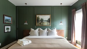 A bedroom with a large bed, a headboard, two wall-mounted lamps, and a framed painting above the bed. - Golfer Paradise - Pool, Sauna, Hot Tub, Putting Green and More! (Pinehurst)