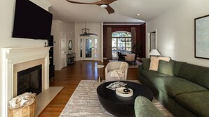 A spacious living room with a fireplace, a green sofa, a coffee table, and a ceiling fan. - Golfer Paradise - Pool, Sauna, Hot Tub, Putting Green and More! (Pinehurst)
