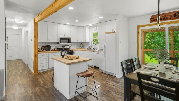 A modern kitchen with white cabinets, a wooden island, and a dining area with a view of greenery. - Stylish Knoxville Retreat w/ Media Room & Patio (Knoxville)