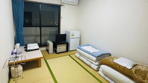 A small hotel room with a bed, a desk, a chair, a television, and a refrigerator. - Villa Iwasawa (Hirono)