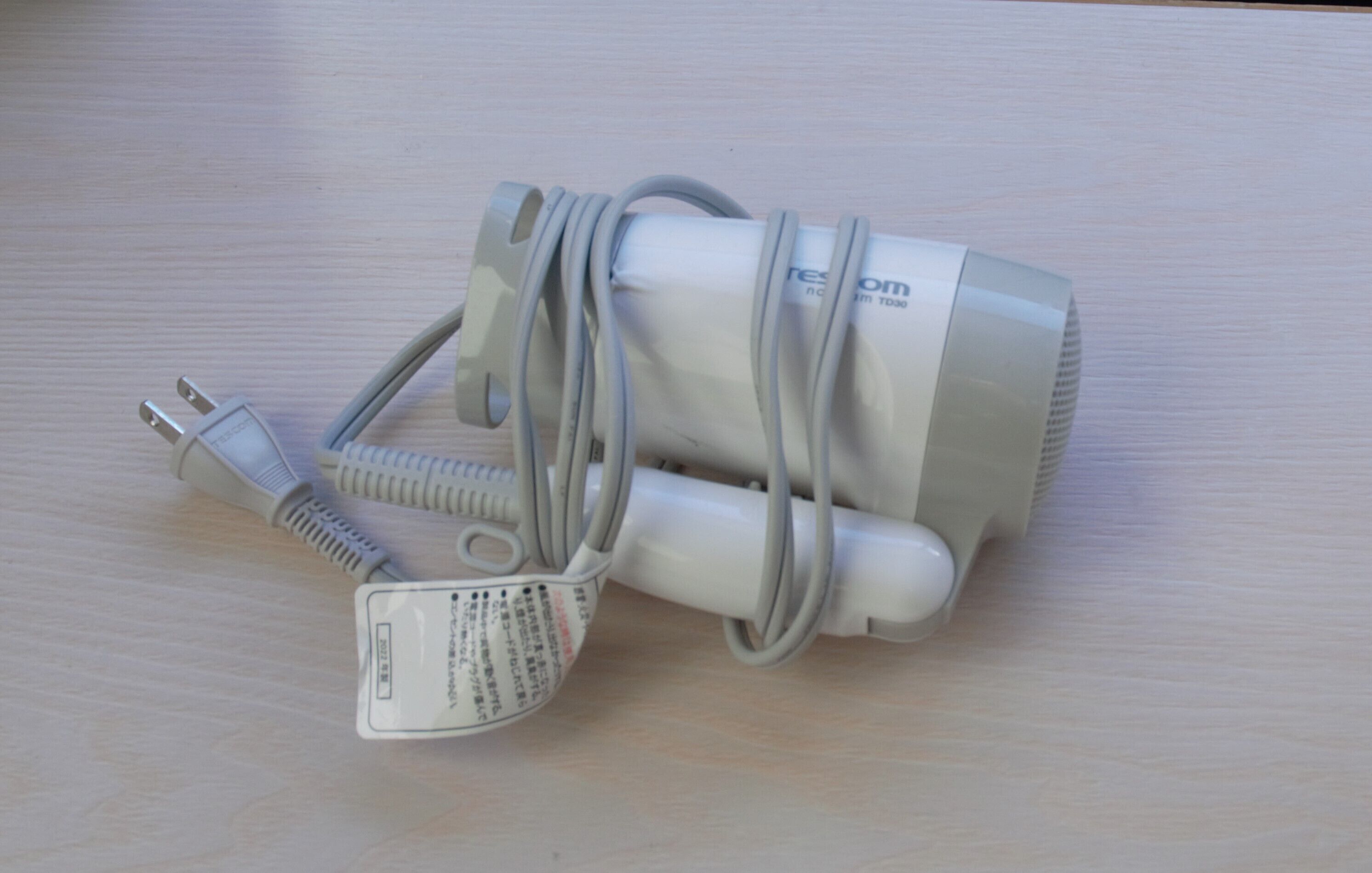 A white power adapter with a plug and a coiled cable on a wooden surface.