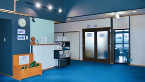 A reception area with a clock, a wooden bench with green objects, a signboard, and a door labeled "BEACH". - Villa Iwasawa (Hirono)