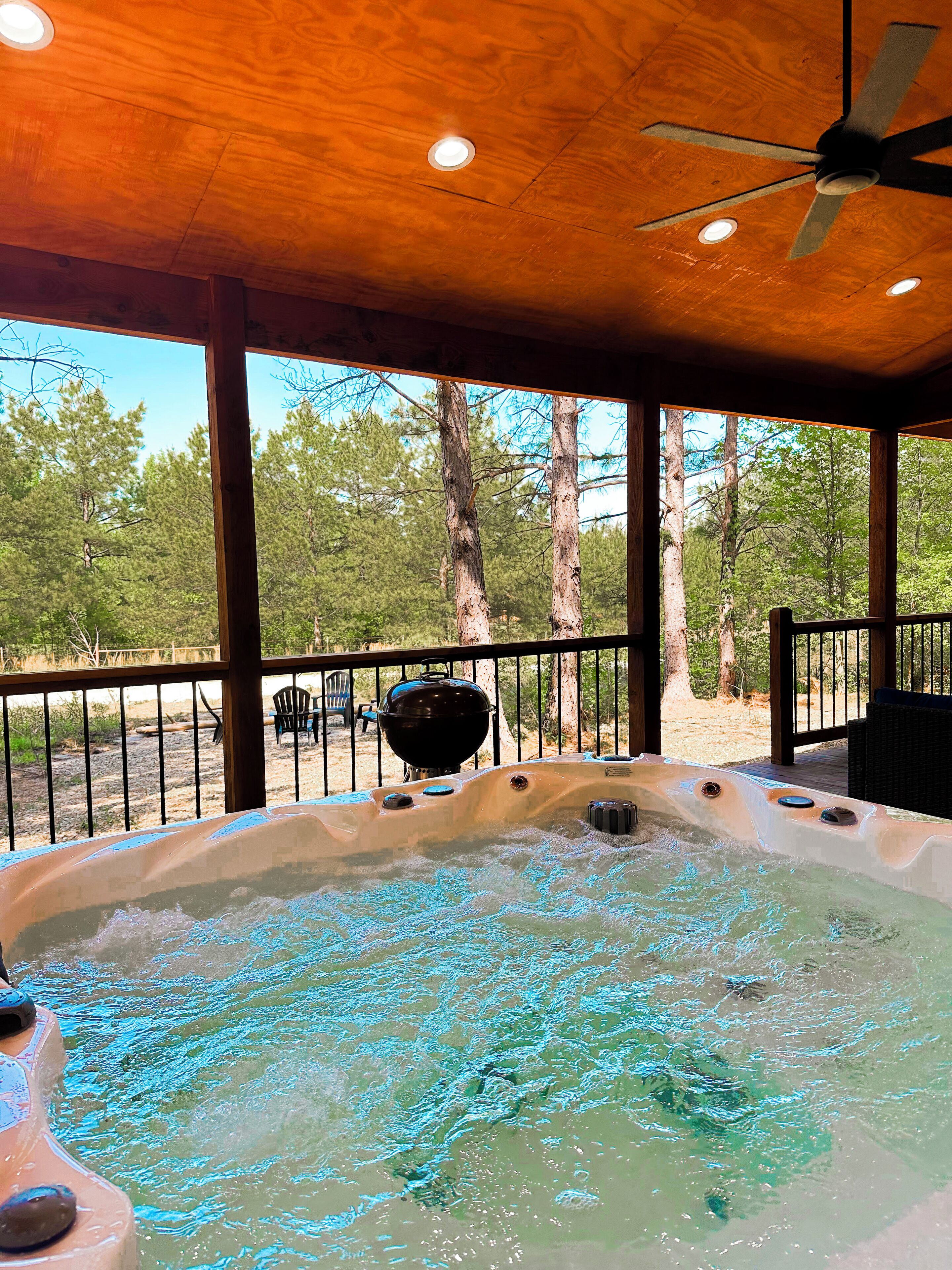 A hot tub with a wooden deck and a view of trees.