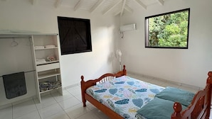 Een slaapkamer met een houten bed, een klein nachtkastje, een kledingkast, een raam en een plafondventilator.