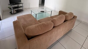 Een woonkamer met een beige bank, een glazen salontafel en een flatscreen televisie op een standaard.