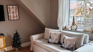 Uma sala de estar acolhedora com um sofá, um pequeno pinheiro de Natal e uma janela com vista para as casas.