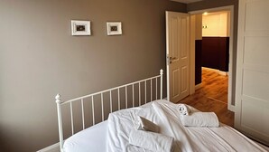 Quarto com uma cama, duas fotos emolduradas na parede e uma porta que dá para outro cômodo.