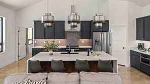 Une cuisine moderne dotée d’un îlot central, de meubles de couleur sombre, d’appareils électroménagers en acier inoxydable et de luminaires suspendus.