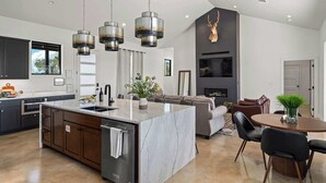Une cuisine moderne dotée d’un îlot en marbre, d’appareils électroménagers en acier inoxydable et de luminaires suspendus.