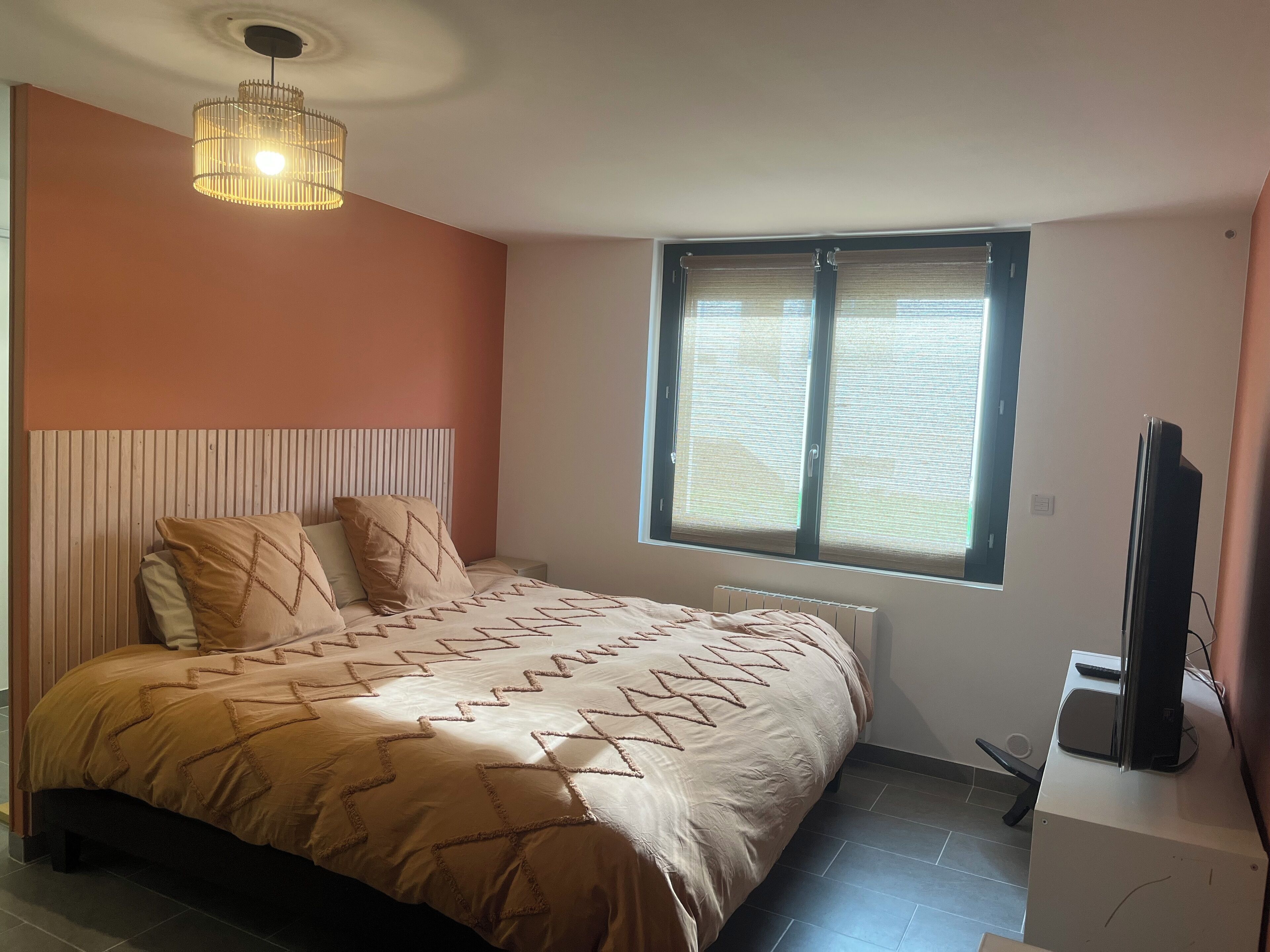 Ein Schlafzimmer mit einem Bett, einer Deckenleuchte, einem Fenster mit Jalousien und einem Fernseher auf einem Schrank.