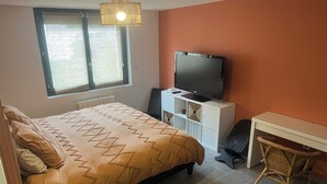 Ein Schlafzimmer mit Bett, Fernseher auf einem Schrank, Schreibtisch und Stuhl.
