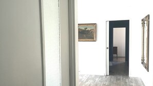 Käytävä, jossa on puulattia, lasikuviollinen ovi ja seinällä oleva kehystetty taulu.