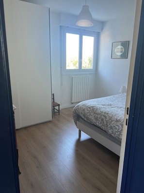 Un dormitorio con cama, ventana, radiador y una silla.