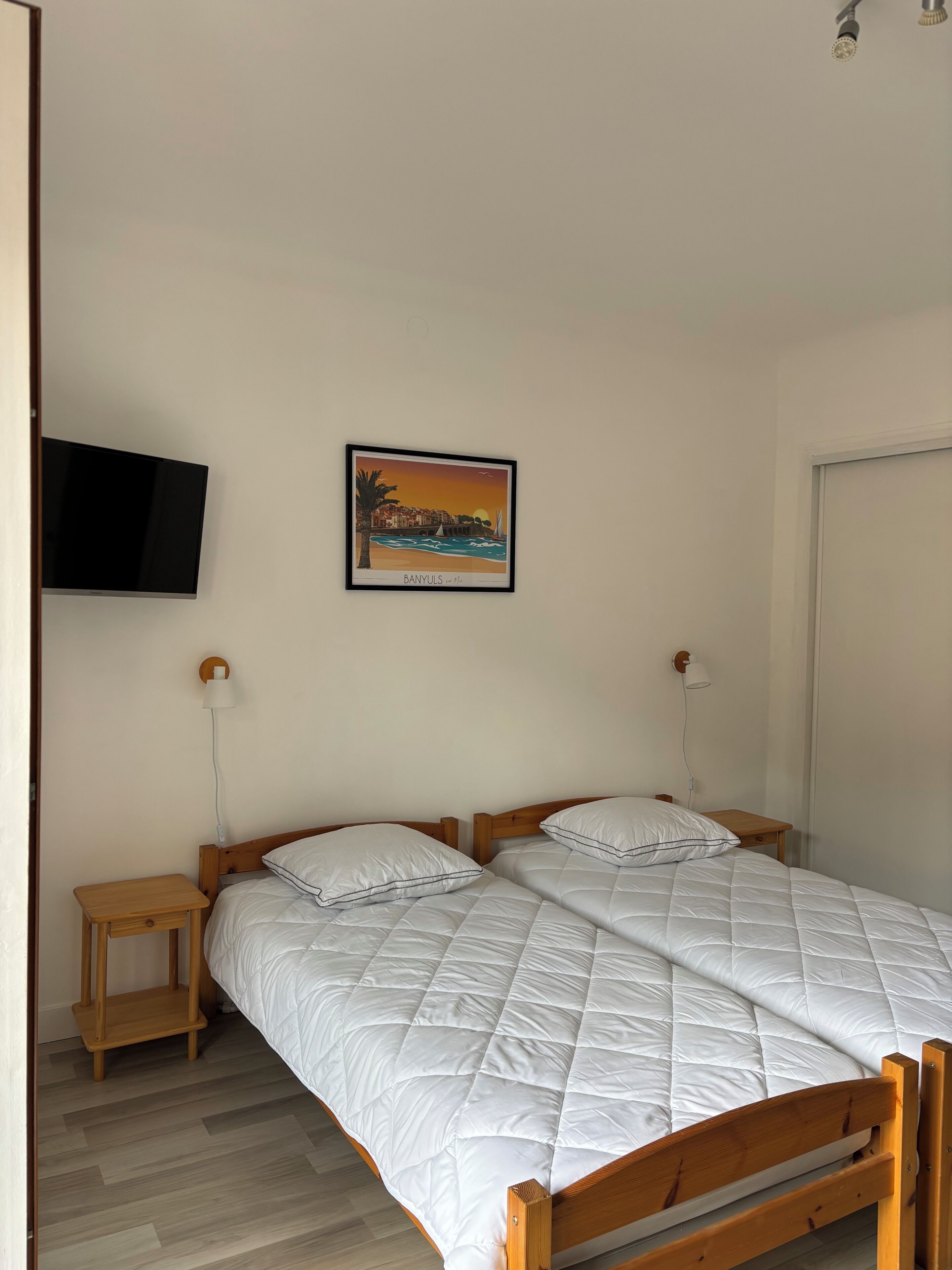 Un dormitorio con dos camas, televisión, un cuadro enmarcado, lámparas de noche y una mesita de noche de madera.