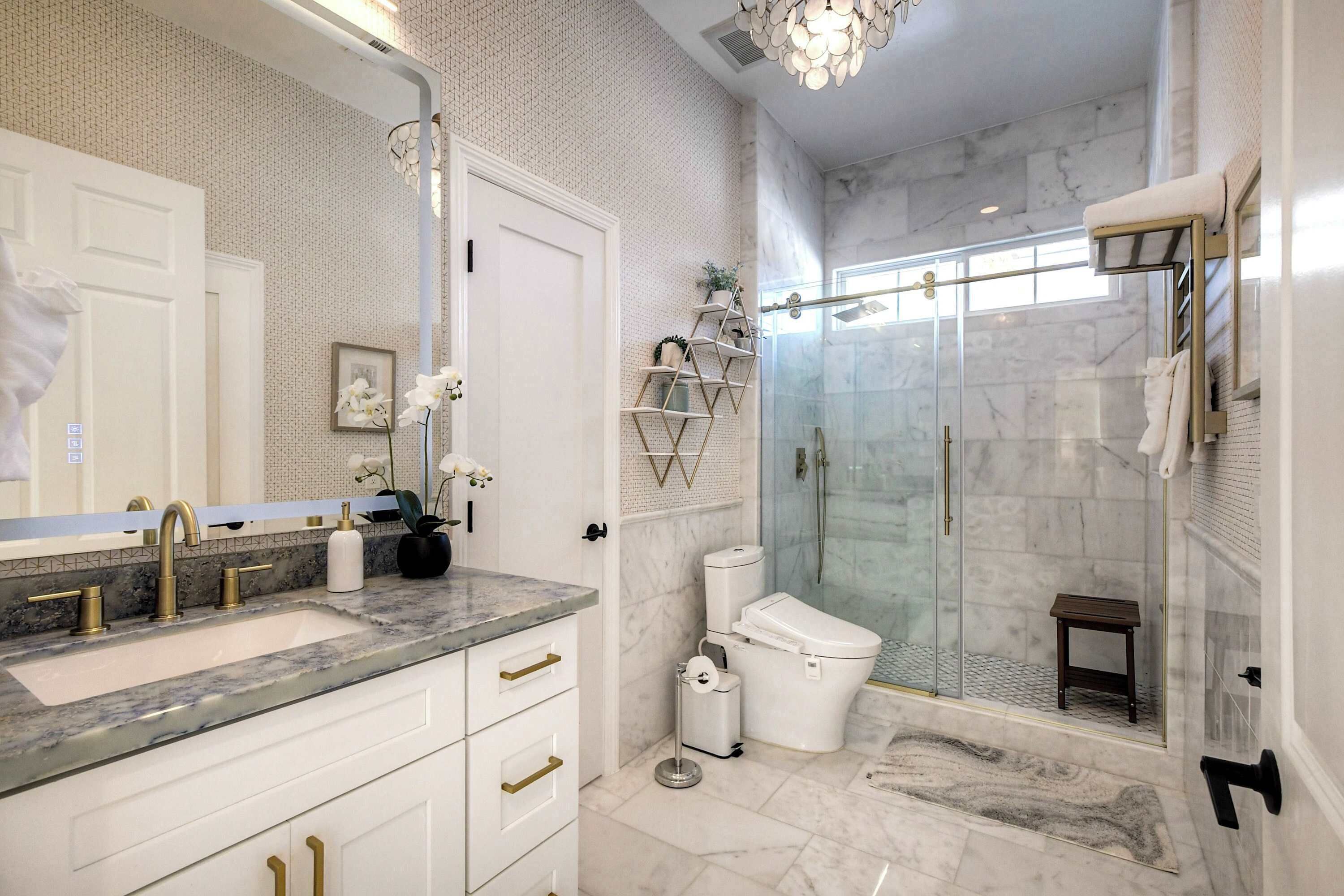 A modern bathroom with a marble sink, a glass shower enclosure, and a white toilet.