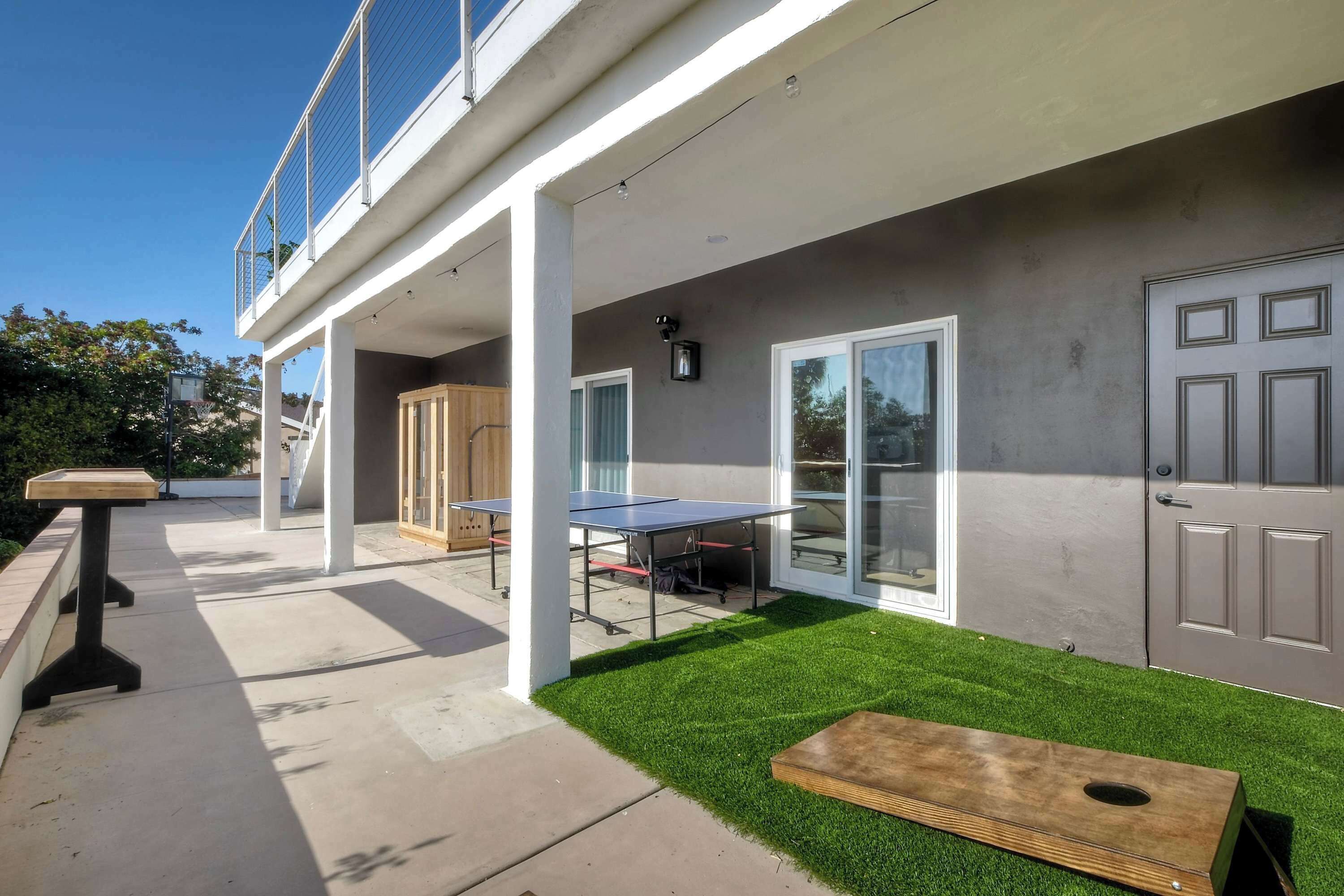 Un patio exterior moderno con mesa de ping pong, banca de madera y un pequeño césped.