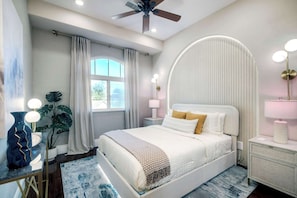 Un dormitorio moderno con cama, lámparas de noche, ventilador de techo, ventana grande con cortinas y una planta decorativa.