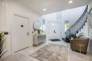 A modern interior with a staircase, a white door, a console table, and a potted plant.