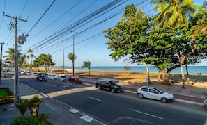 Eine Küstenstraße mit geparkten Autos, ein Strand im Hintergrund und Palmen säumen die Straße.