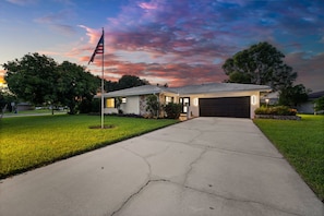 A residential house with a driveway leading to a garage, surrounded by a well-maintained lawn and trees. - Sun-Kissed Modern Oasis with Private Heated Pool (Fort Myers)