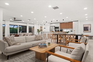 A modern living room with a sofa, coffee table, and dining area with chairs. - Sun-Kissed Modern Oasis with Private Heated Pool (Fort Myers)