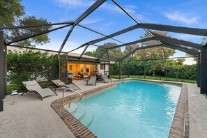 A swimming pool with a covered patio area, lounge chairs, and a view of the surrounding greenery. - Sun-Kissed Modern Oasis with Private Heated Pool (Fort Myers)