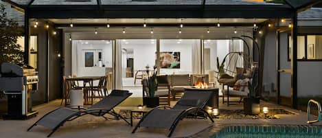 A poolside area with lounge chairs, a barbecue grill, and a fire pit.