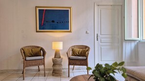 A room with two wicker chairs, a small round table with a lamp, and a framed abstract painting on the wall.