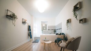 Ein modernes Wohnzimmer mit einer Couch, einem Sessel, einem kleinen runden Tisch und einer Küchenzeile im Hintergrund.