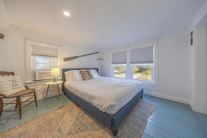 A bedroom with a bed, a chair, a nightstand with a lamp, and a window with blinds.