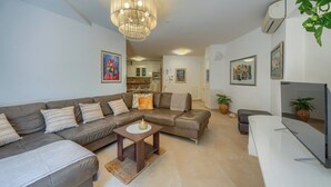 A modern living room with a sectional sofa, a coffee table, a TV, and a chandelier. - A2 comfortable apartment with terrace and garden, 4 min walk to Znjan beach (Split)