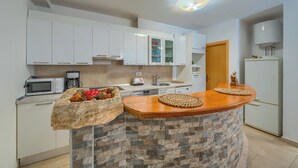 A modern kitchen with white cabinets, a microwave, a coffee maker, and a stone island with woven placemats. - A2 comfortable apartment with terrace and garden, 4 min walk to Znjan beach (Split)