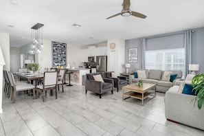 A modern living room with a dining area, grey sofas, a coffee table, and a kitchen in the background.