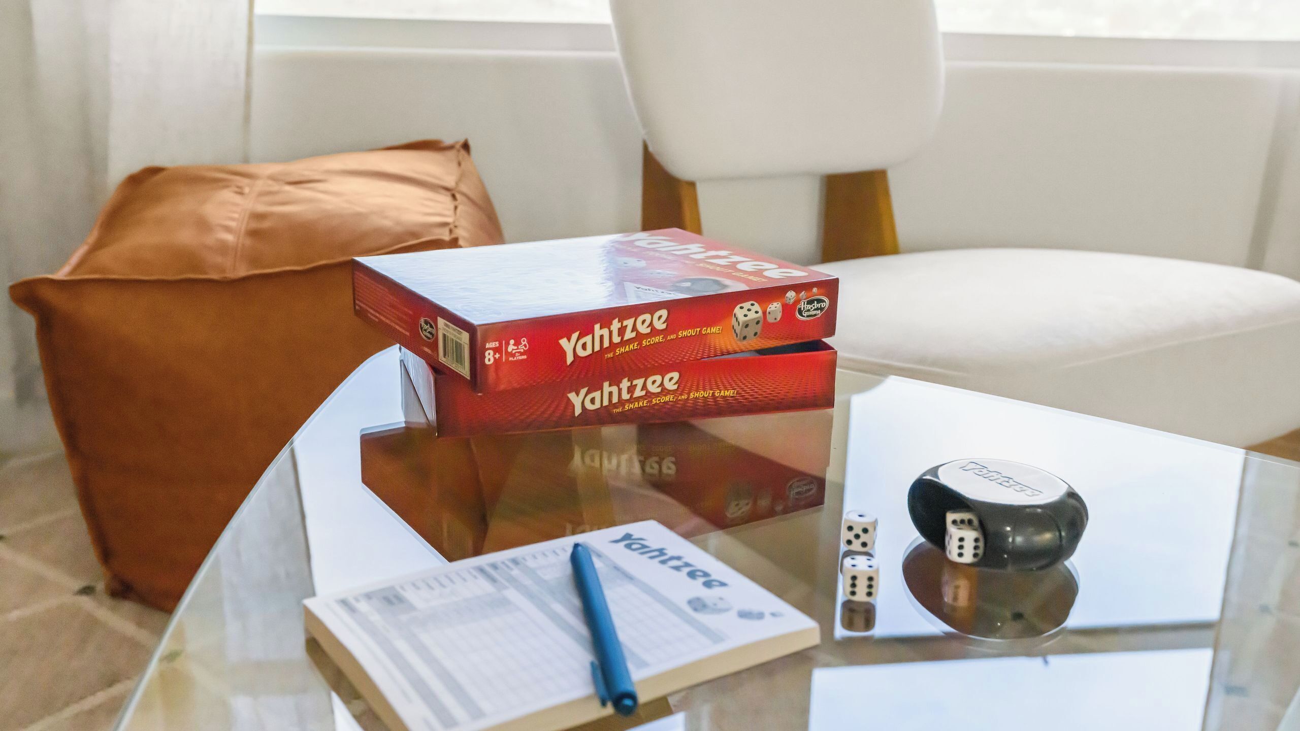 Une table en verre avec un jeu de société, des dés et un stylo.