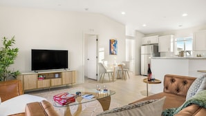 Ein modernes Wohnzimmer mit Flachbildfernseher, Glastisch, Sofa und Essbereich mit Tisch und Stühlen.
