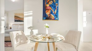 A modern hotel room with a glass dining table, white chairs, a bed with a striped blanket, and a large painting on the wall. - Modern Ranch Home w/ Vineyard Views & Patio Pergola Shimla Syrah by Avantstay (Paso Robles)