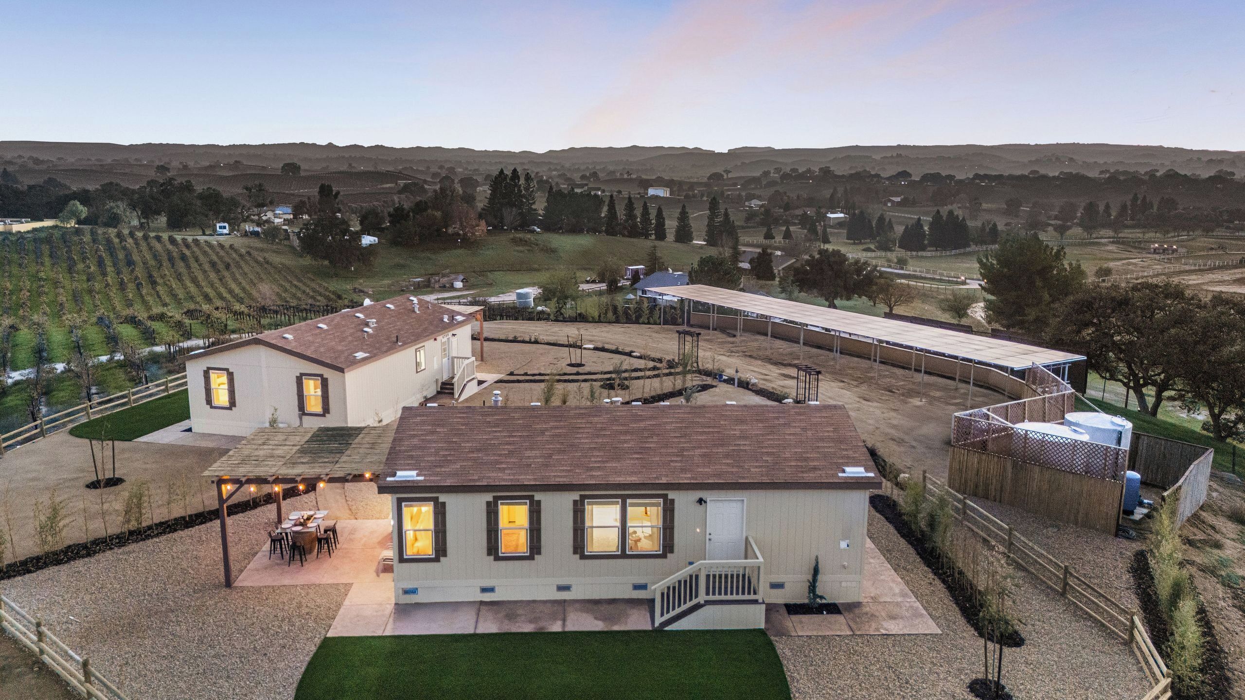 A large, single-story building with a flat roof, surrounded by a well-maintained lawn and a vineyard in the background.