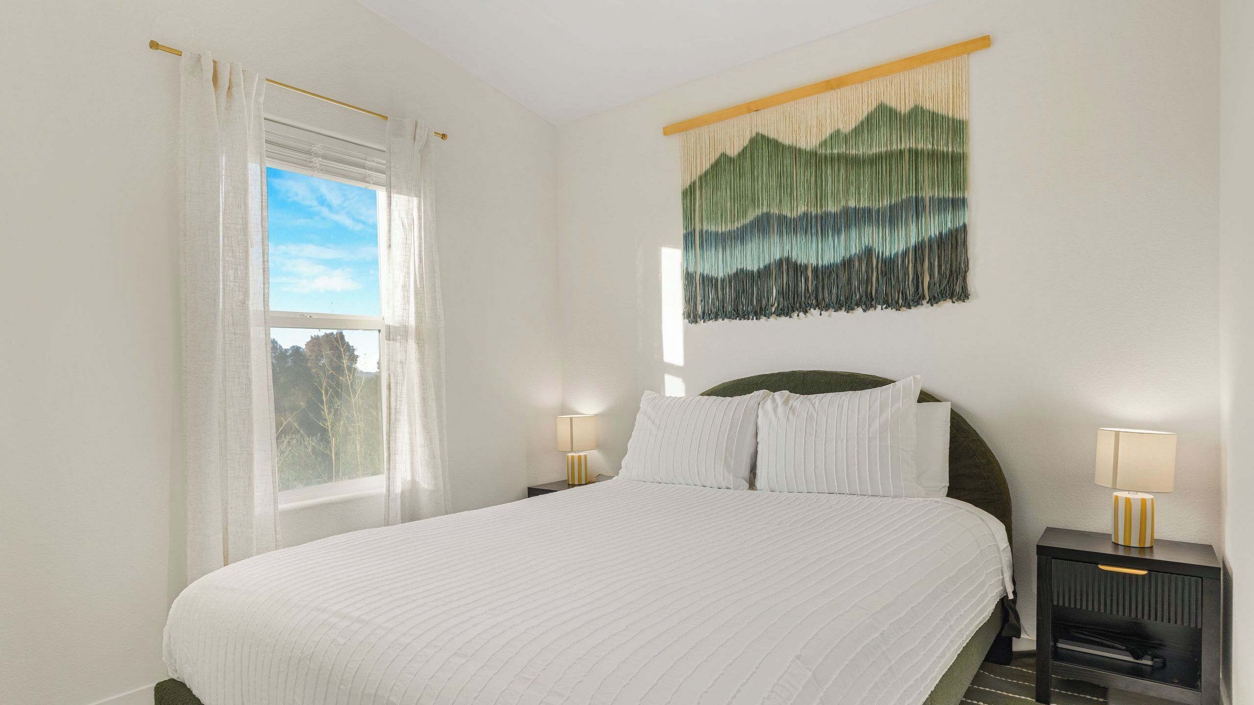 A neatly made bed with white linens, a green headboard, and two bedside tables with lamps.