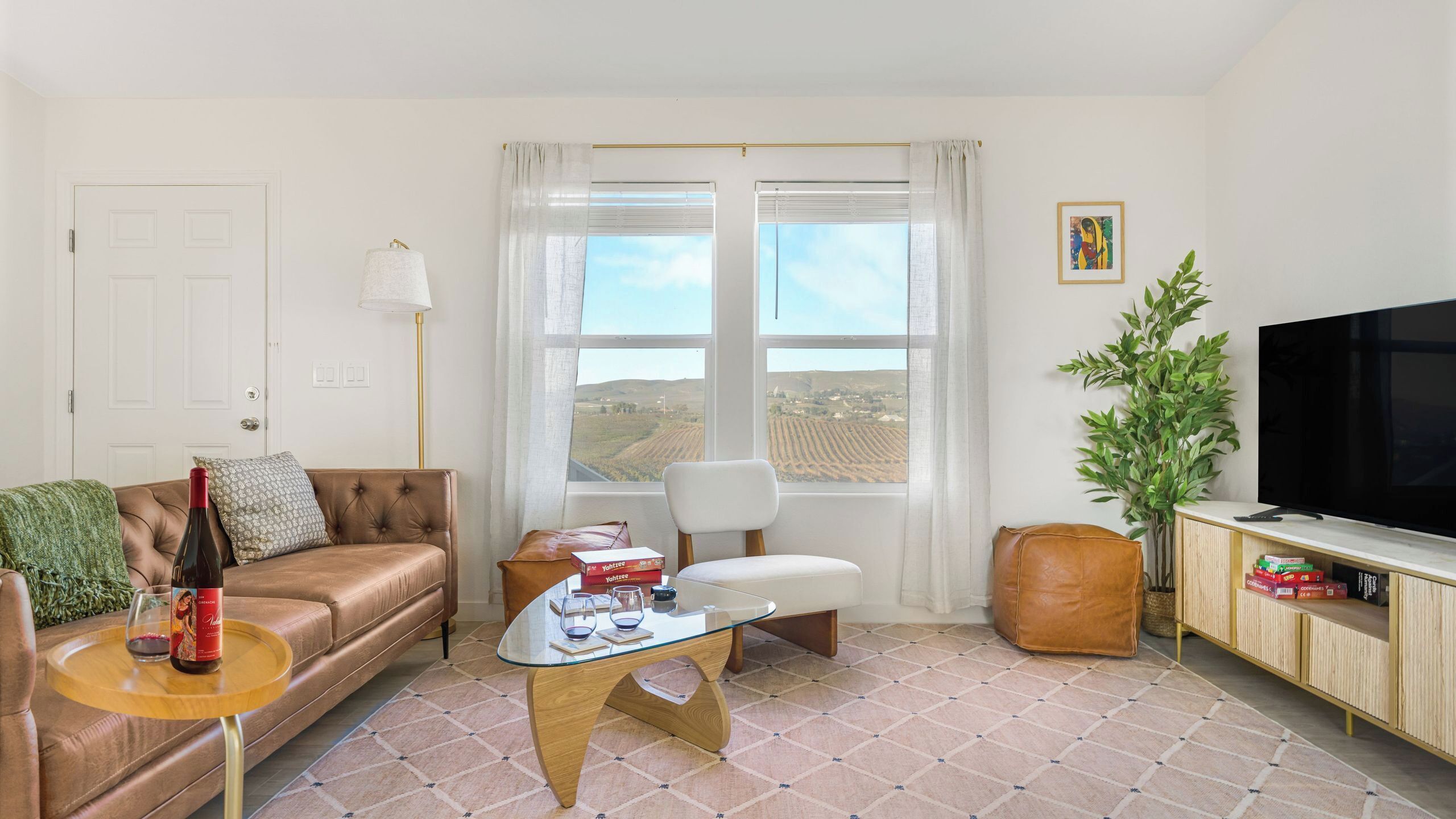 A living room with a sofa, a glass coffee table, a TV, a window with a view, and a plant.